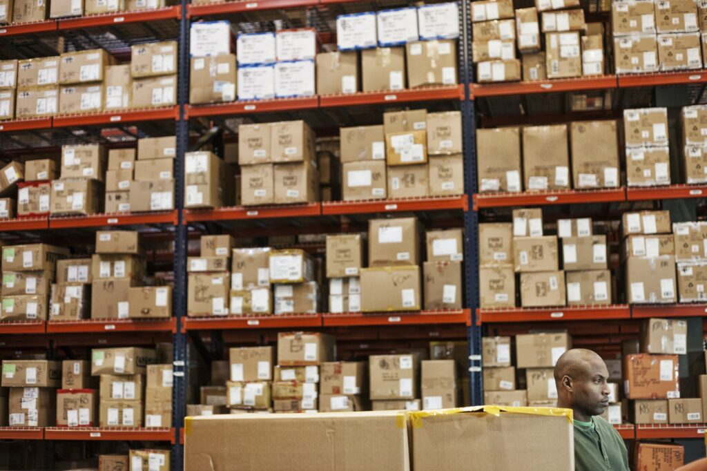 African American warehouse worker checking inventory next to large racks of cardboard boxes holding